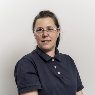 Porträt von Manja Klockow aus DIE ZAHNARZTPRAXIS Stralsund, im dunkelblauen Poloshirt und mit Brille vor hellem Hintergrund, verantwortlich für Abrechnung und Verwaltungsaufgaben der Praxis.