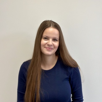 Porträt von ZFA Denise Lüdemann aus DIE ZAHNARZTPRAXIS Stralsund, im dunkelblauen Oberteil vor hellem Hintergrund, freundlich in die Kamera blickend und in der Praxis ausgebildet.