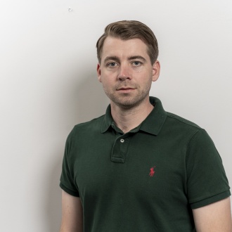 Porträt von Praxisleiter Stefan Motz aus DIE ZAHNARZTPRAXIS Stralsund, im dunkelgrünen Poloshirt vor hellem Hintergrund stehend und ruhig in die Kamera blickend.