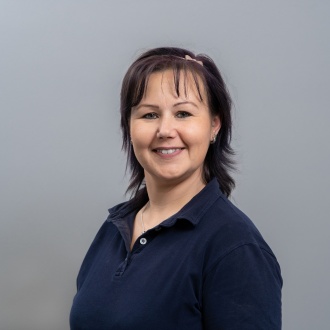 Porträt von Nicole Wesslowski aus DIE ZAHNARZTPRAXIS Stralsund, erfahrene ZFA im dunkelblauen Poloshirt vor grauem Hintergrund, freundlich lächelnd und leicht seitlich zur Kamera gewandt.